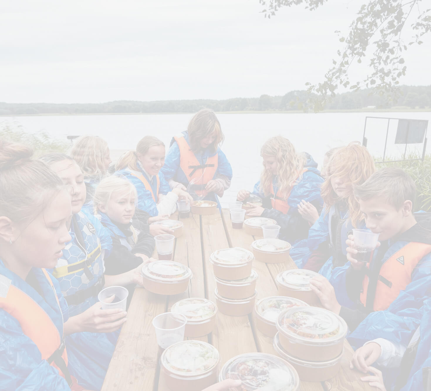 Dzieci w kamizelkach ratunkowych siedzące przy stole i odpakowujące catering.